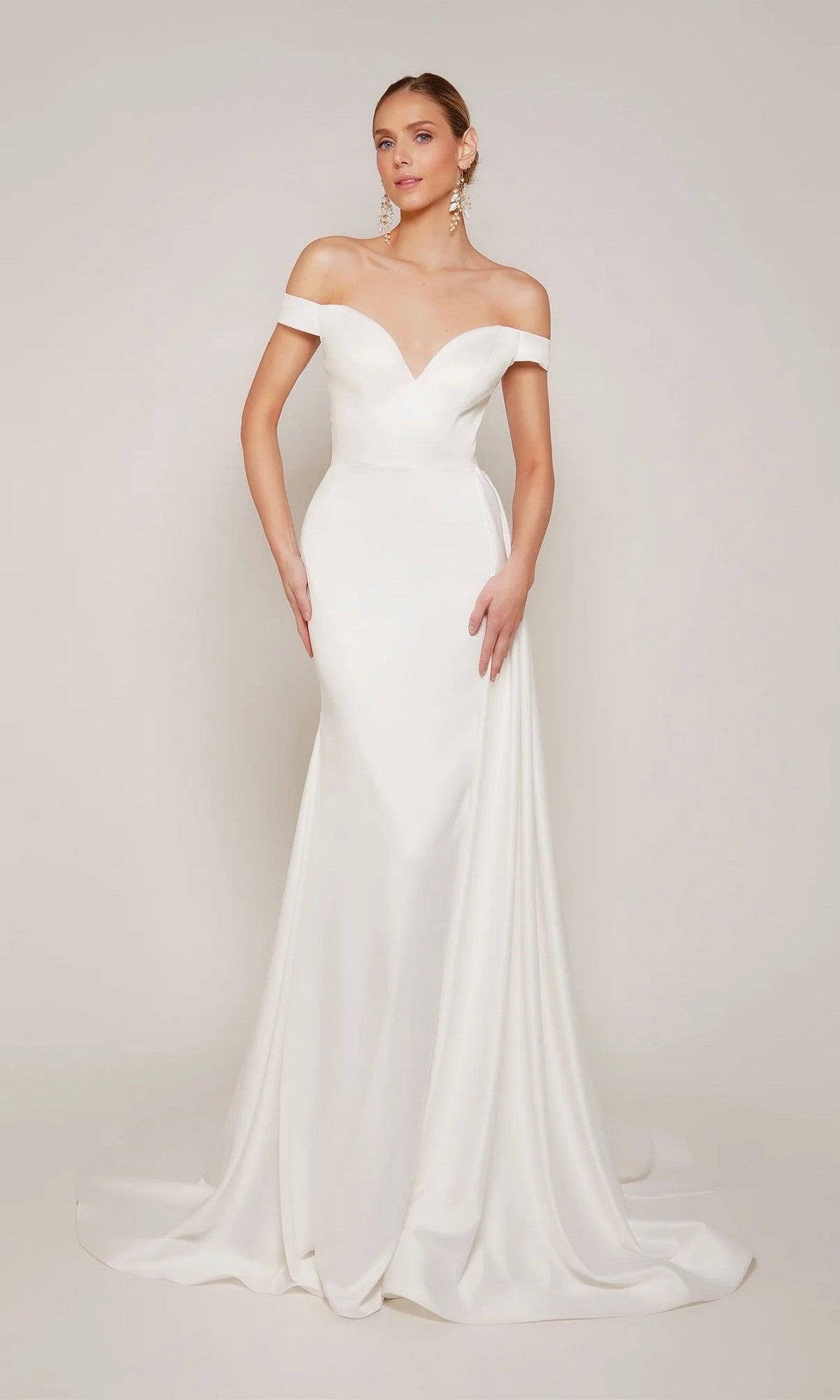 A woman poses against a plain backdrop in the Alyce 7098 long formal dress, featuring a fitted silhouette, diamond white color, off-the-shoulder sweetheart neckline, and slight train.